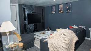 Un salon moderne avec un téléviseur à écran plat, des canapés sombres, une table basse et des œuvres d’art encadrées accrochées au mur.