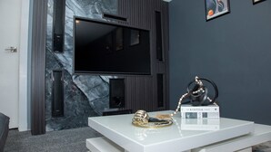 Un salon moderne doté d’un grand téléviseur à écran plat fixé sur un mur sombre, d’un meuble de rangement blanc agrémenté d’objets décoratifs et d’un mur à la texture évoquant le marbre.