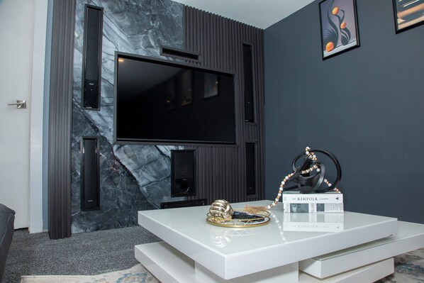 Un salon moderne doté d’un grand téléviseur à écran plat fixé sur un mur sombre, d’un meuble de rangement blanc agrémenté d’objets décoratifs et d’un mur à la texture évoquant le marbre.