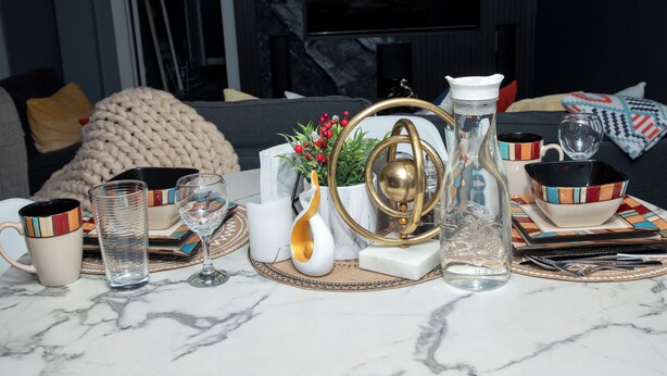 Une table en marbre sur laquelle sont disposés divers objets, notamment un verre transparent, un vase blanc, un objet décoratif doré et une tasse à rayures.