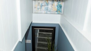 Un escalier étroit avec une main courante, un pot de fleurs et un tableau accroché au mur.