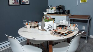 Un espace repas avec une table ronde, des chaises blanches et un coin café.