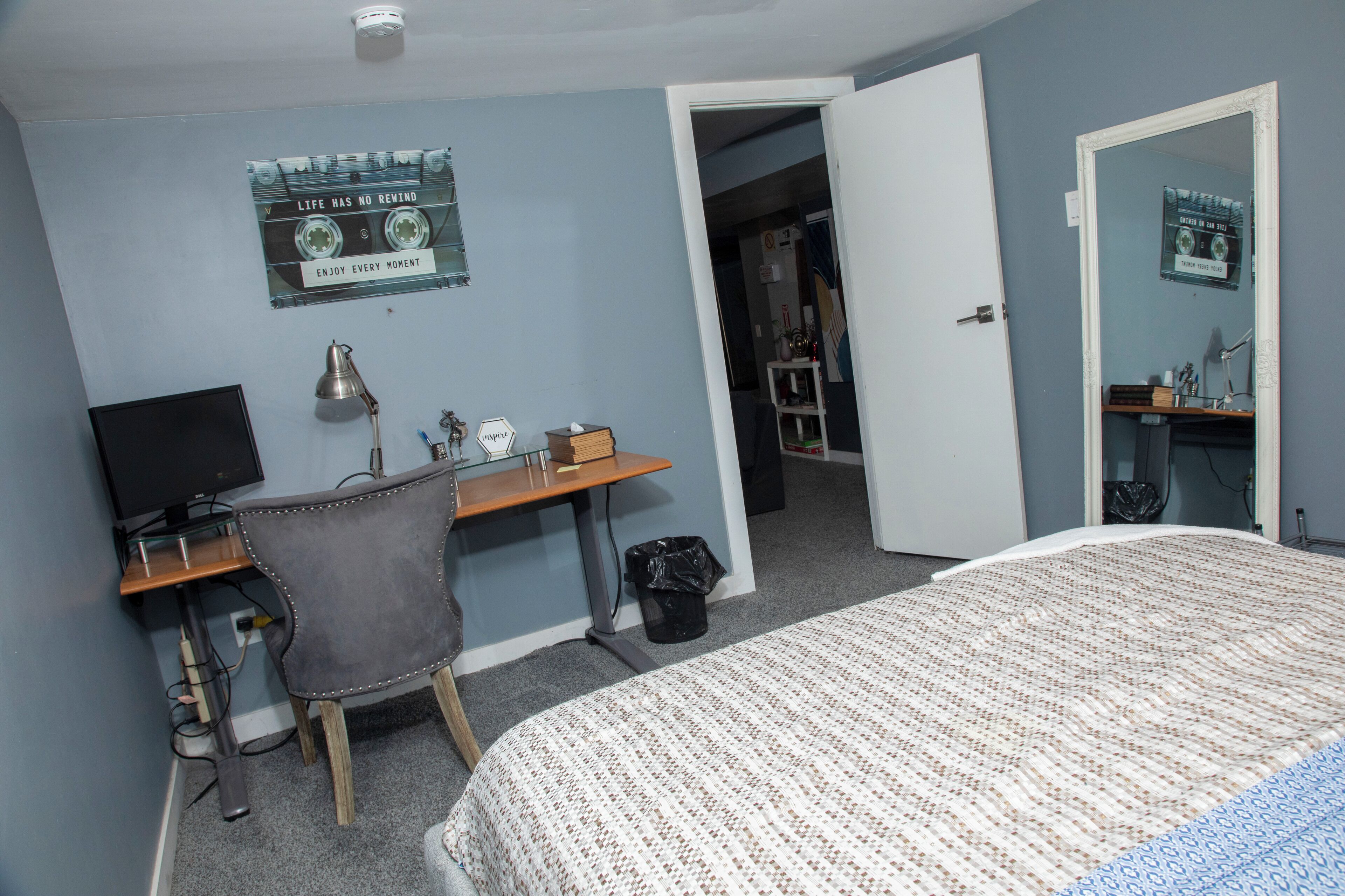 Un dormitorio con una cama, un escritorio con computadora, una silla y una puerta que da a otra habitación.