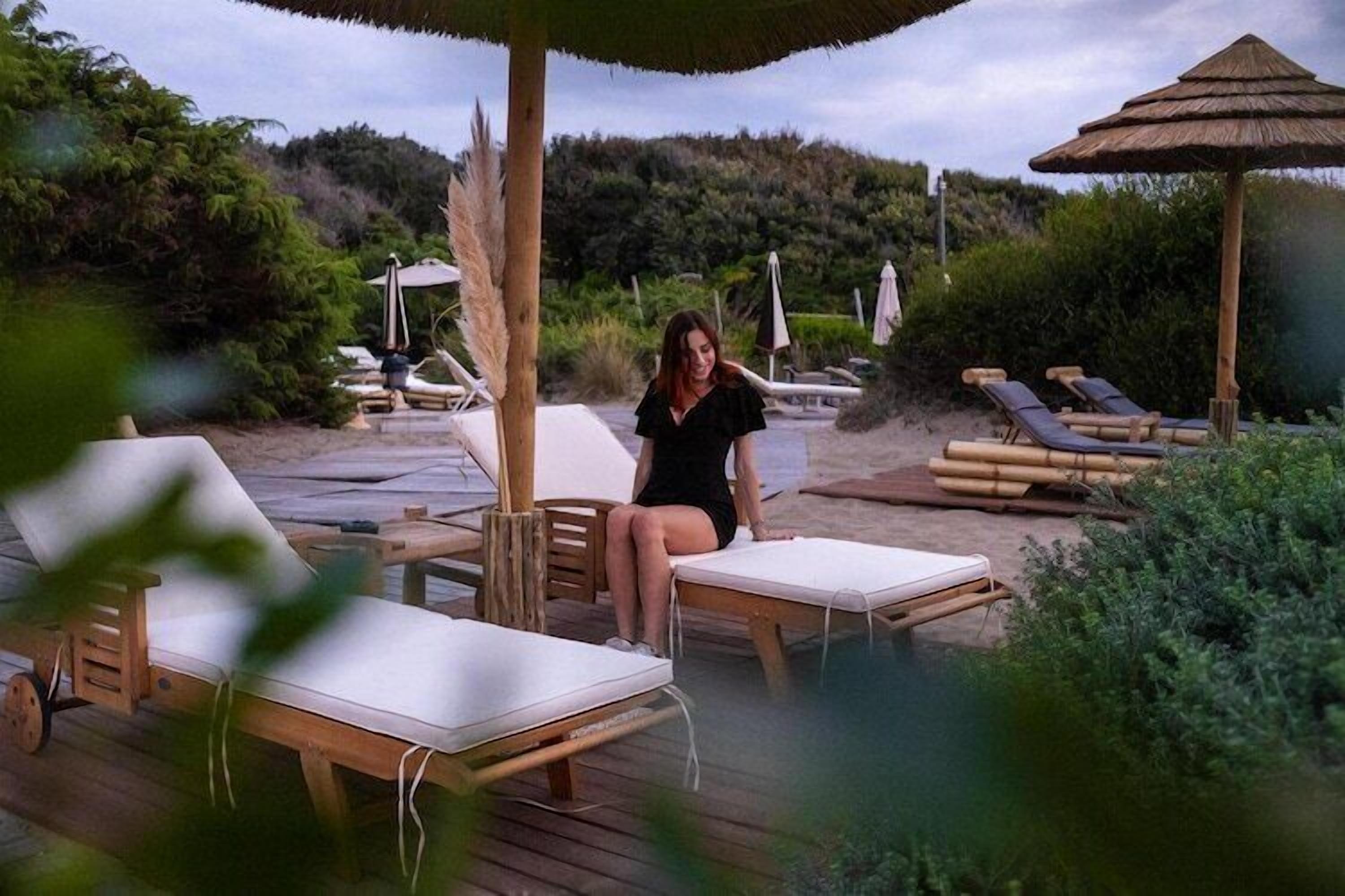 A wooden deck with lounge chairs and a thatched umbrella, surrounded by greenery.