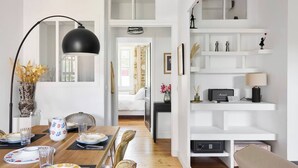 Una sala de estar moderna con comedor, estanterías blancas y una lámpara de pie negra.