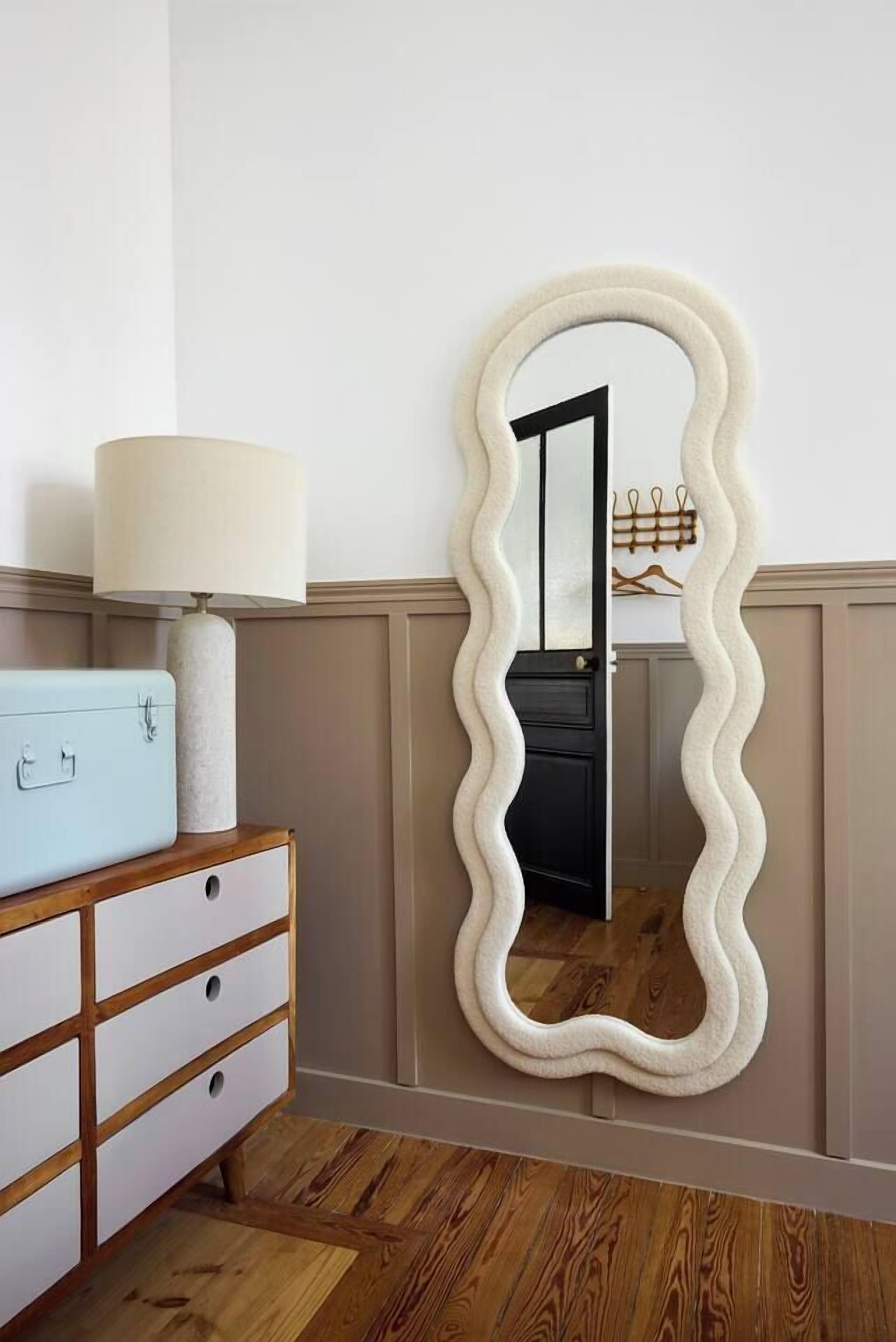 Et værelse med en trækommode, en lampe og et bølgeformet spejl på væggen.