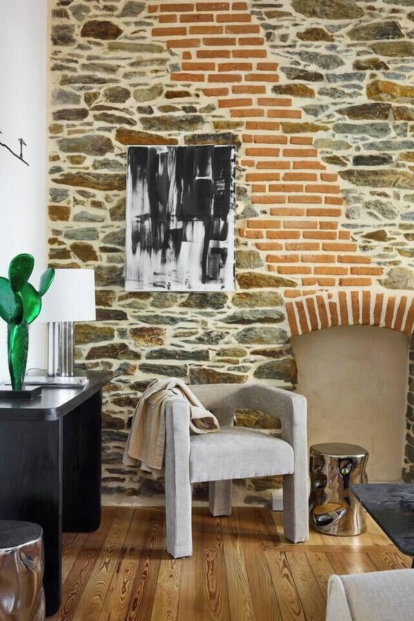 A room with a stone wall, a modern chair, a lamp, and a table.