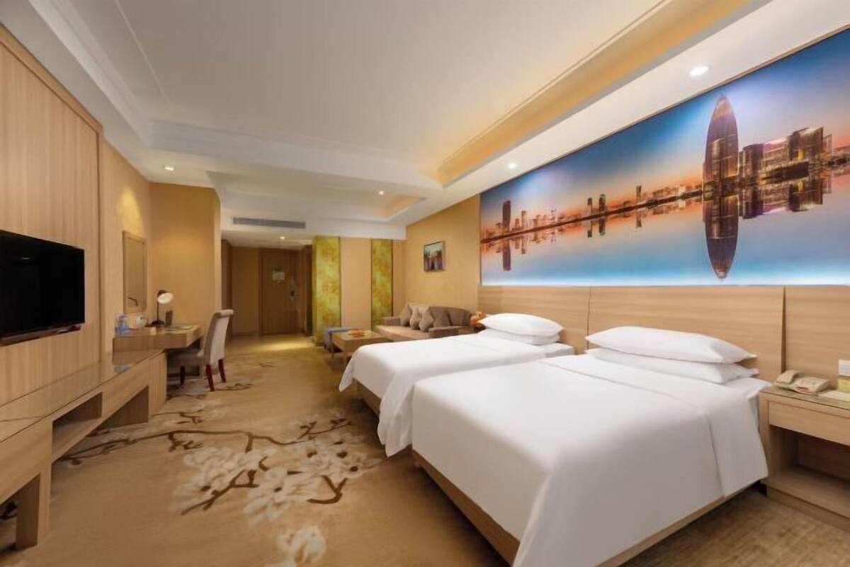 A hotel room with two beds, a TV, a desk, and a cityscape mural.