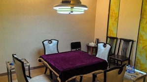 Un salón de conferencias con una mesa, cuatro sillas, un mantel morado, una lámpara en el techo y un espejo en la pared.