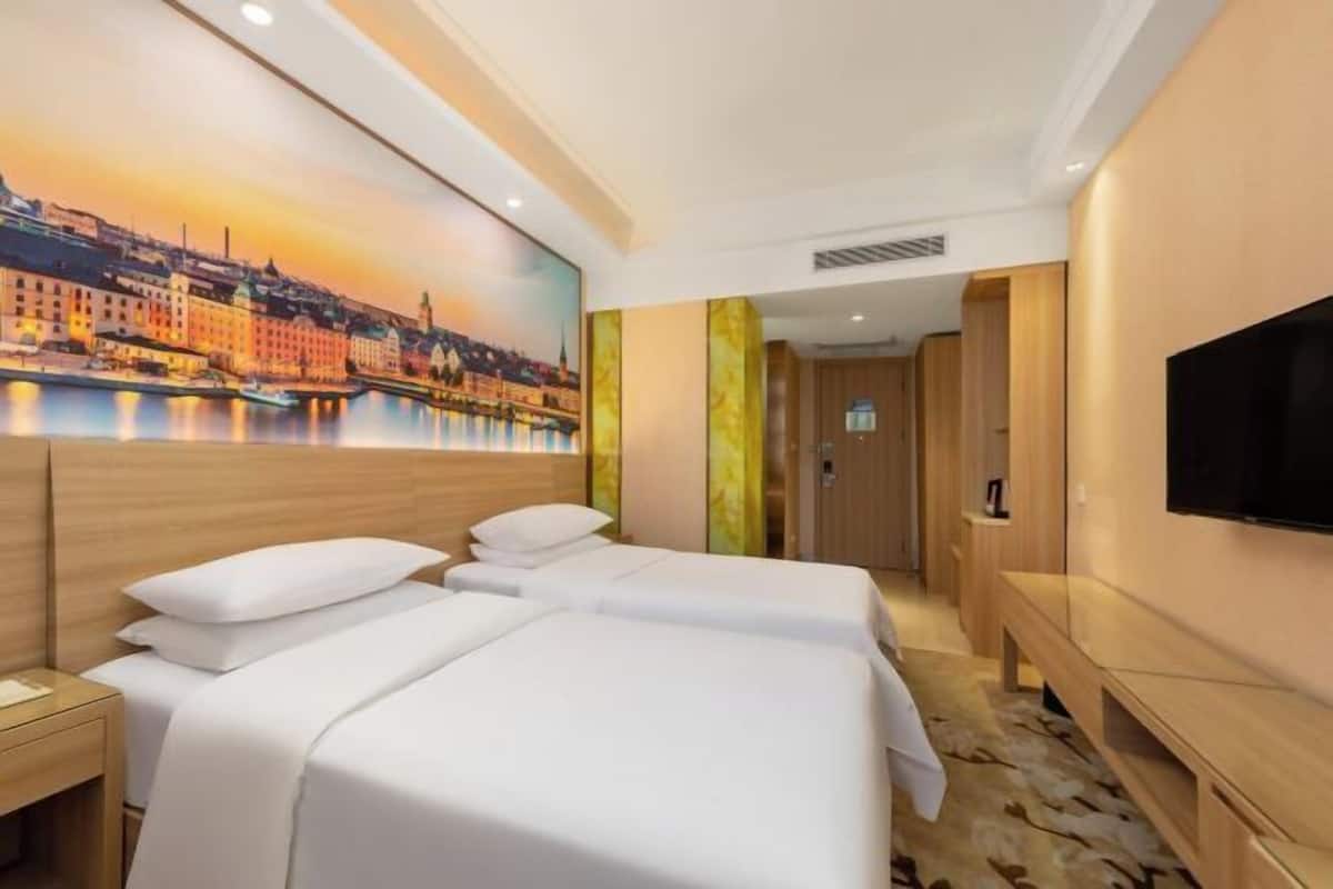 A hotel room with two beds, a large painting of a cityscape, a flat-screen TV, and wooden paneling.