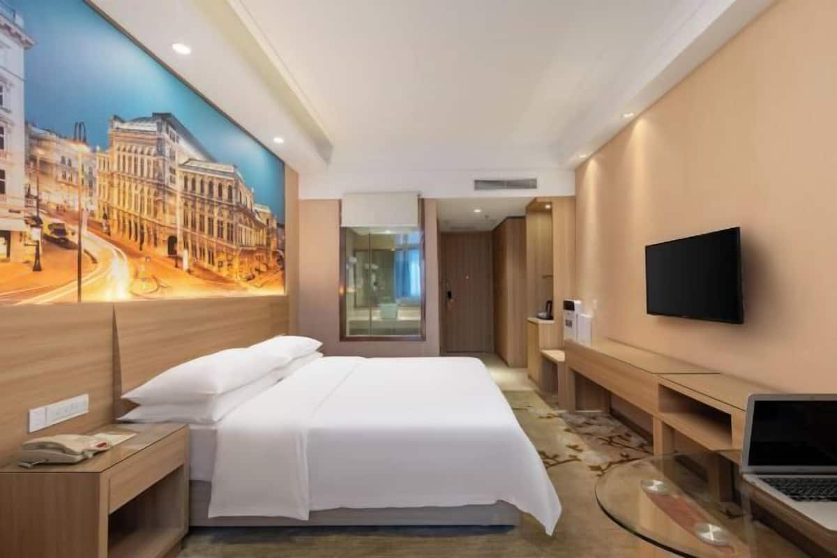 A hotel room with a bed, a TV, a desk, and a painting of a cityscape.