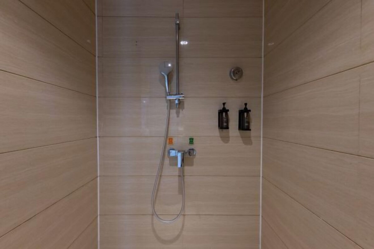 A shower with a handheld showerhead, a wall-mounted control panel, and a soap dispenser.