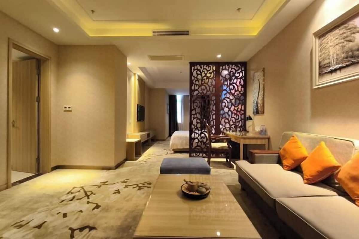 A hotel room with a sofa, a coffee table, a decorative screen, and a painting on the wall.