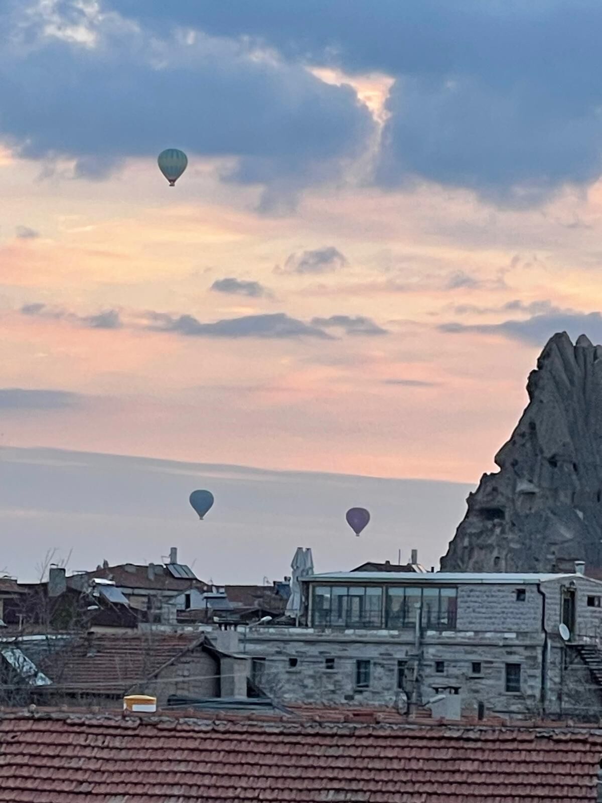 A cityscape with buildings, a prominent rock formation, and three hot air balloons in the sky.
