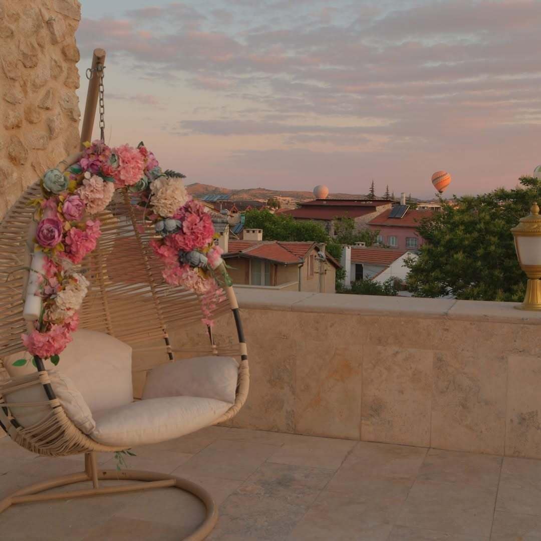 A wicker swing chair with a floral arrangement, a stone wall, and a view of buildings in the background.