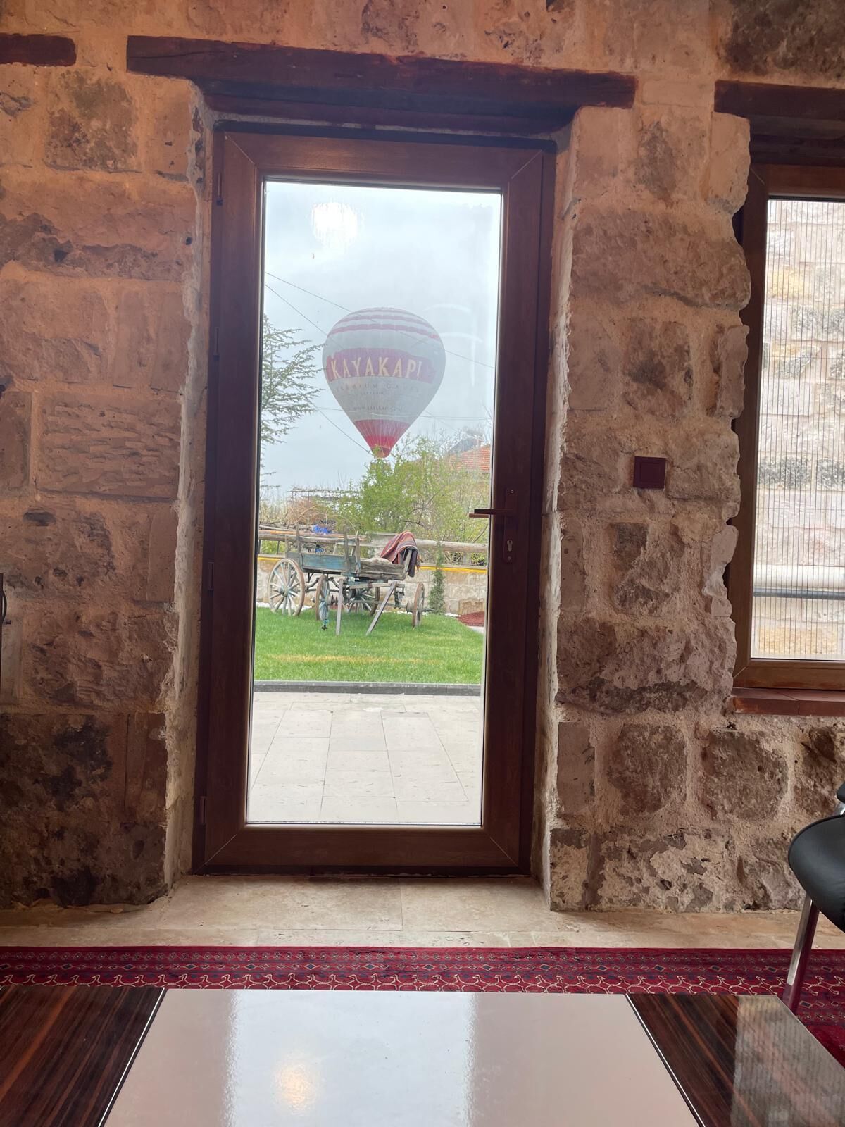 Una habitación con pared de piedra, puerta de madera y vista a un globo aerostático.