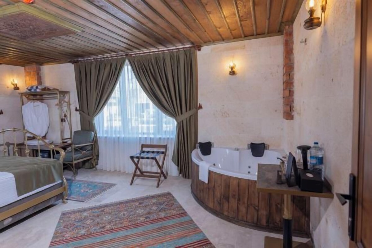 A room with a bed, a chair, a small table, a bathtub, and a window with curtains.