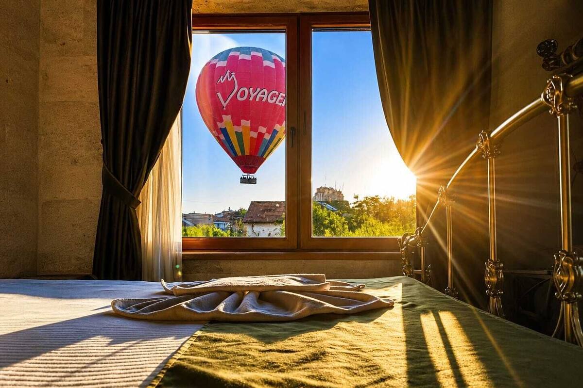 Een kamer met een bed, een raam met gordijnen, een luchtballon buiten en een lamp aan de rechterkant.