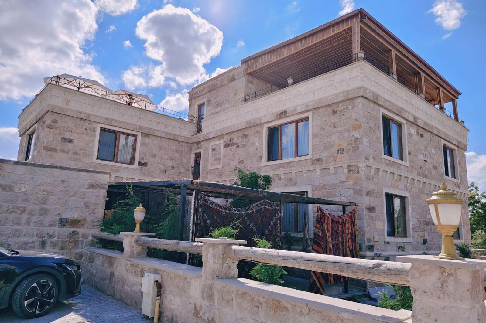 Un edificio de piedra con múltiples ventanas y balcones, un área exterior cubierta y un coche estacionado al frente.
