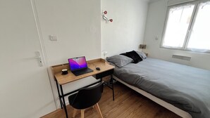 A bedroom with a bed, a desk with a laptop, a chair, and a window. - Bright 3-room apartment in the center of Royan, 3-minute walk from the beach and port. (Royan)