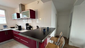 A modern kitchen with red cabinets, a stainless steel countertop, and a bar area with stools. - Bright 3-room apartment in the center of Royan, 3-minute walk from the beach and port. (Royan)