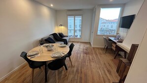 A dining area with a round table set for four, a sofa, and a TV in a corner. - Bright 3-room apartment in the center of Royan, 3-minute walk from the beach and port. (Royan)