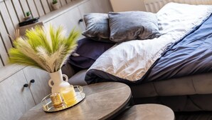 Une chambre à coucher moderne avec un lit, des oreillers, une table de chevet avec un vase et un plateau, et un radiateur.