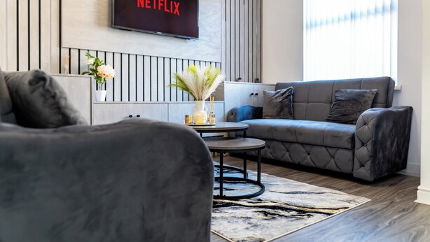 Un salon moderne avec un canapé gris, une table basse et un téléviseur fixé au mur qui affiche « NETFLIX ».