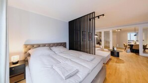 Een moderne hotelkamer met een groot bed, een nachtkastje, een kleine ronde tafel en een zithoek met een fauteuil.