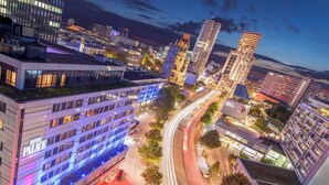 Een modern hotel met meerdere verdiepingen, een terras op het dak en uitzicht op de omliggende stadsgezicht.