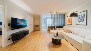 Een moderne woonkamer met een flatscreen televisie, een ronde salontafel en een witte bank.