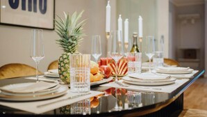 Een eettafel gedekt met borden, glazen en een ananas als middelpunt, met kaarsen en een fles op de achtergrond.