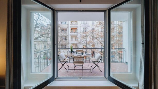 Een balkon met een tafel en stoelen, met uitzicht op een binnenplaats met gebouwen.