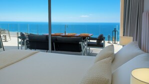 A balcony with a view of the ocean, a dining table with chairs, and a bed with pillows. - Apartment Sleeps 4 With Gym & Spa (Benalmádena)