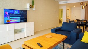 A modern living room with a flat-screen TV on a white cabinet, a blue sofa, a wooden coffee table, and a yellow cushion. - Apartment Sleeps 4 With Gym & Spa (Benalmádena)