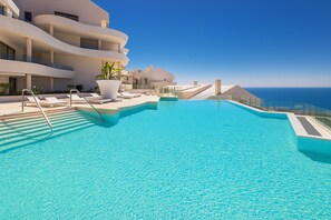Une piscine offrant une vue dégagée sur l’océan, entourée de bâtiments blancs dotés de balcons.