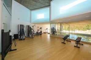 Ein geräumiger Fitnessraum mit unterschiedlichen Trainingsgeräten, großen Fenstern und Blick auf Grünflächen.