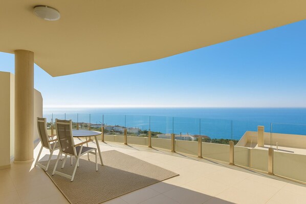 Un balcon avec vue sur la mer, une table et deux chaises.