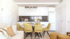 A modern living room with a sofa, two armchairs, a coffee table, and a dining area with a table and chairs.