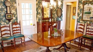 A dining room with a wooden table, chairs, a chandelier, and floral wallpaper.