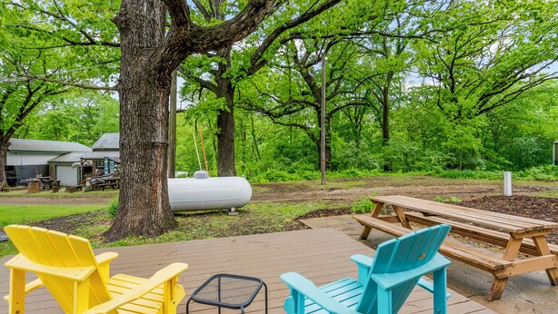 Una terraza de madera con dos sillas Adirondack, una mesa de picnic y un barril metálico.