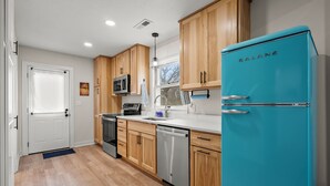 Una cocina moderna con armarios de madera, un lavavajillas de acero inoxidable y un refrigerador Galanz color turquesa.