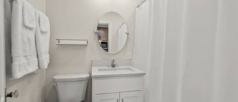 A bathroom with a toilet, sink, mirror, and shower curtain.