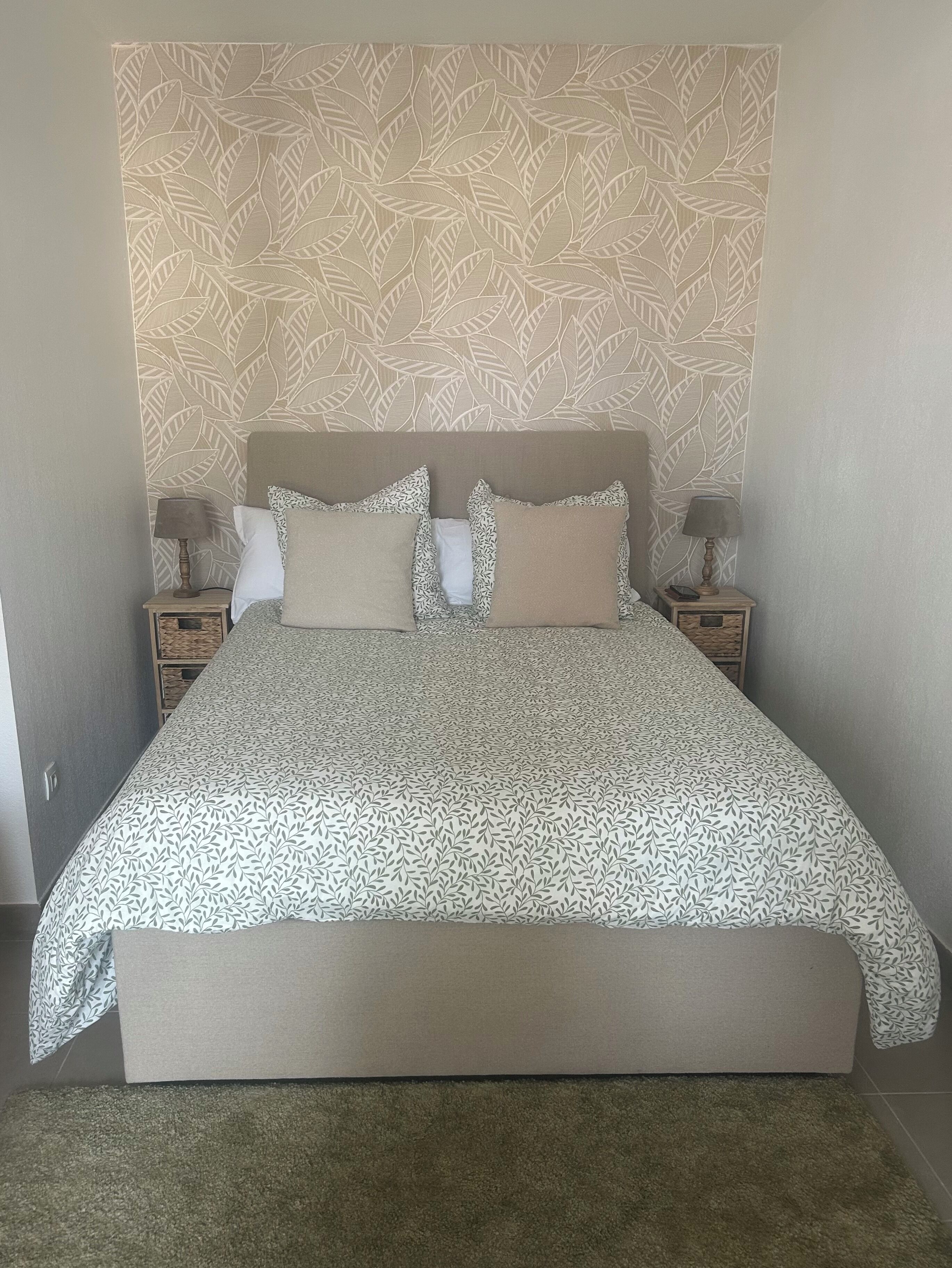 A bedroom with a bed, two nightstands, a patterned headboard, and a carpeted floor.