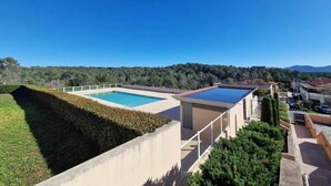 A rooftop with two swimming pools, surrounded by greenery and a clear blue sky.