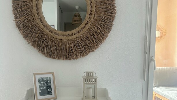 A white console table with a round mirror, a framed photo, and a lantern. There are two woven baskets under the table and a wicker basket to the right.