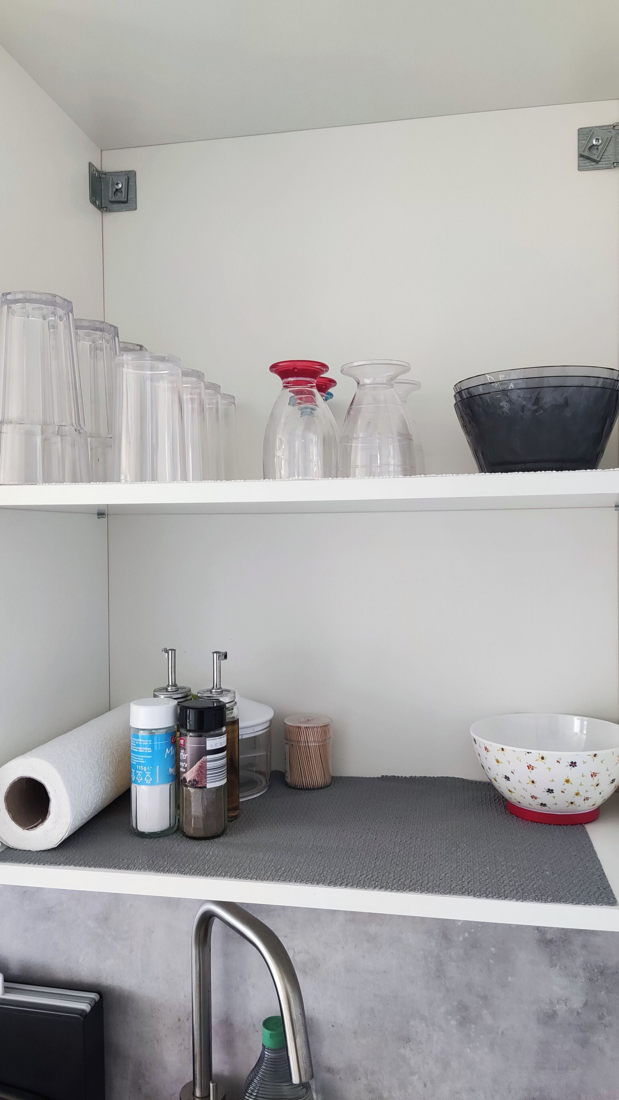 Una cocina con estantes blancos, un rollo de toallas de papel, saleros y pimenteros, un cesto de basura pequeño y un tazón.