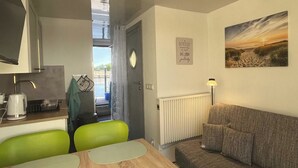 A compact living space with a kitchenette, a dining area with a table and chairs, a sofa, a radiator, and a wall with a framed quote.