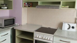A compact kitchen with a microwave, stove, and a small oven. There are green shelves above the counter holding various items.