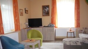 A living room with a television, a radio, a green chair, a blue chair, and a sofa.